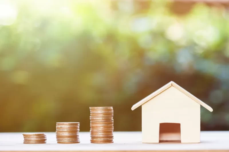 A rising stack of pennies near a home purchased with an asset-based mortgage