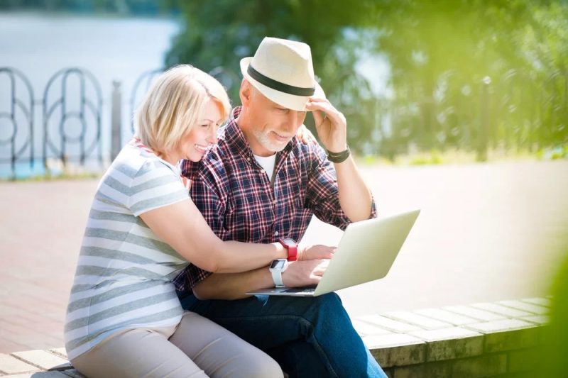 A middle-aged couple corresponding with a reverse mortgage broker on a laptop outdoors